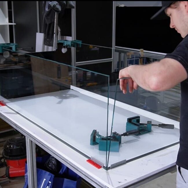 Man placing a glass panel into its position, ready for it to be siliconed to make an aquarium