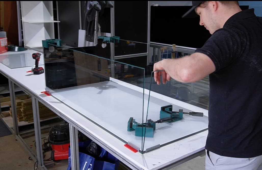 Man placing a glass panel into its position, ready for it to be siliconed to make an aquarium